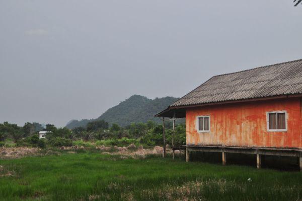 Trang Province House on stilts in a grassy field Mountain in the background