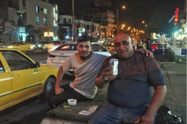 Two men from Baghdad having a drink on the street 