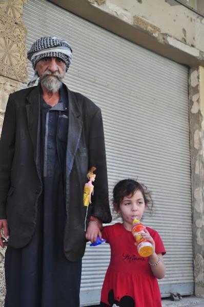 grandfather holding granddaughter by hand while on walk through the destroyed city of mosul in iraq