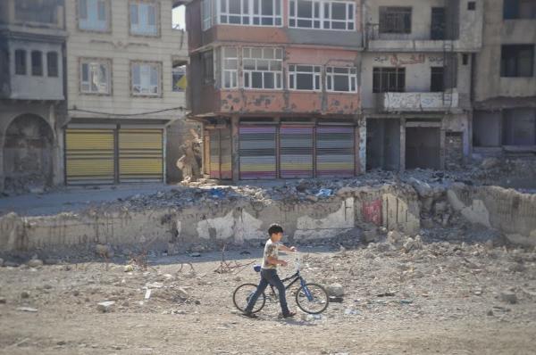 small boy pushing bicycle through the rubble in mosul, iraq