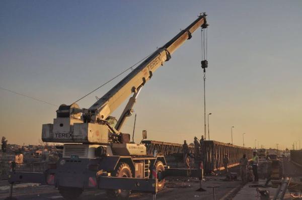 crane and workers repairing broken bridge in mosul iraq