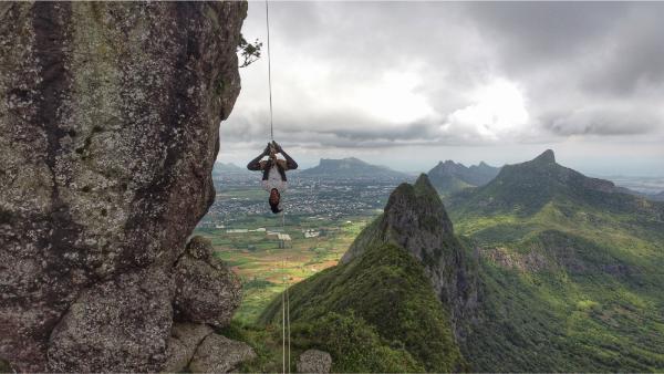 man hanging like spiderman from cliff on pieter both mountain in mauritius