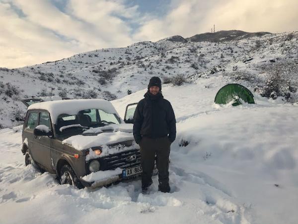 man standing infront of a lada niva and a camping tent in the snow Menaxhuar Nature Reserve, Korce County, Albania in the winter