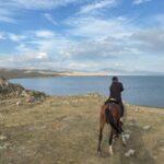 horse rider looking at the view of song kul lake in kyrgyzstan from atop a hill