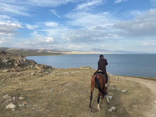 horse rider looking at the view of song kul lake in kyrgyzstan from atop a hill