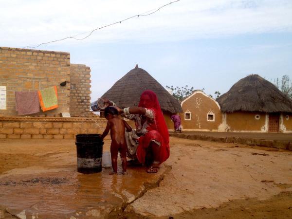 indian woman washing a boy in desert village in rajasthan 