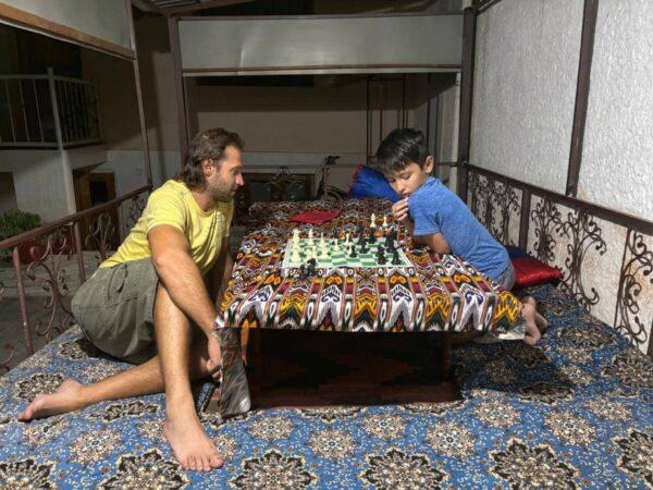 Greek tourist playing chess with uzbek children's champion in optimist guesthouse in samarkand