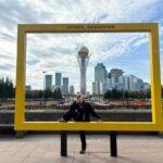 girl posing in yellow frame in front of Astana’s futuristic downtown