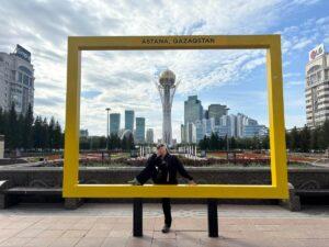 girl posing in yellow frame in front of Astana’s futuristic downtown