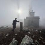 photo of a man with the sun dimly visible through the fog on top of mount telethrion on euboea island, greece