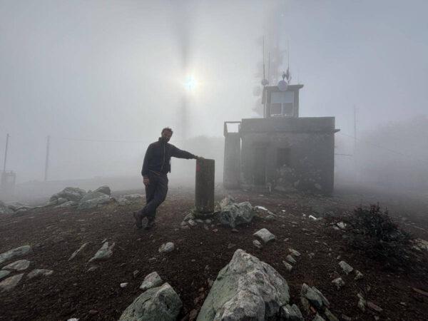 photo of a man with the sun dimly visible through the fog on top of mount telethrion on euboea island, greece