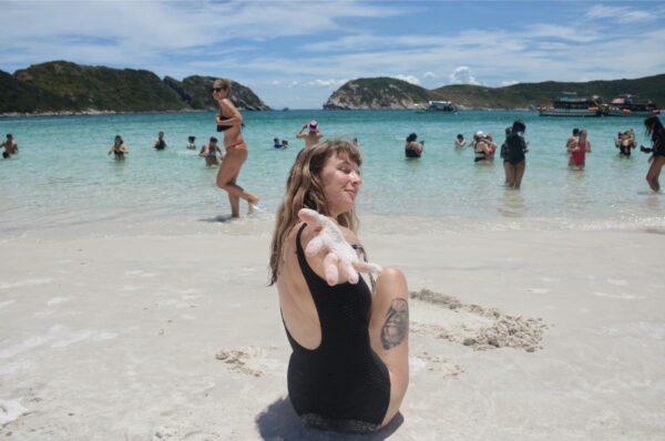 girl sitting on white sand before the sea at praia do farol beach on ilha de cabo frio island in brazil
